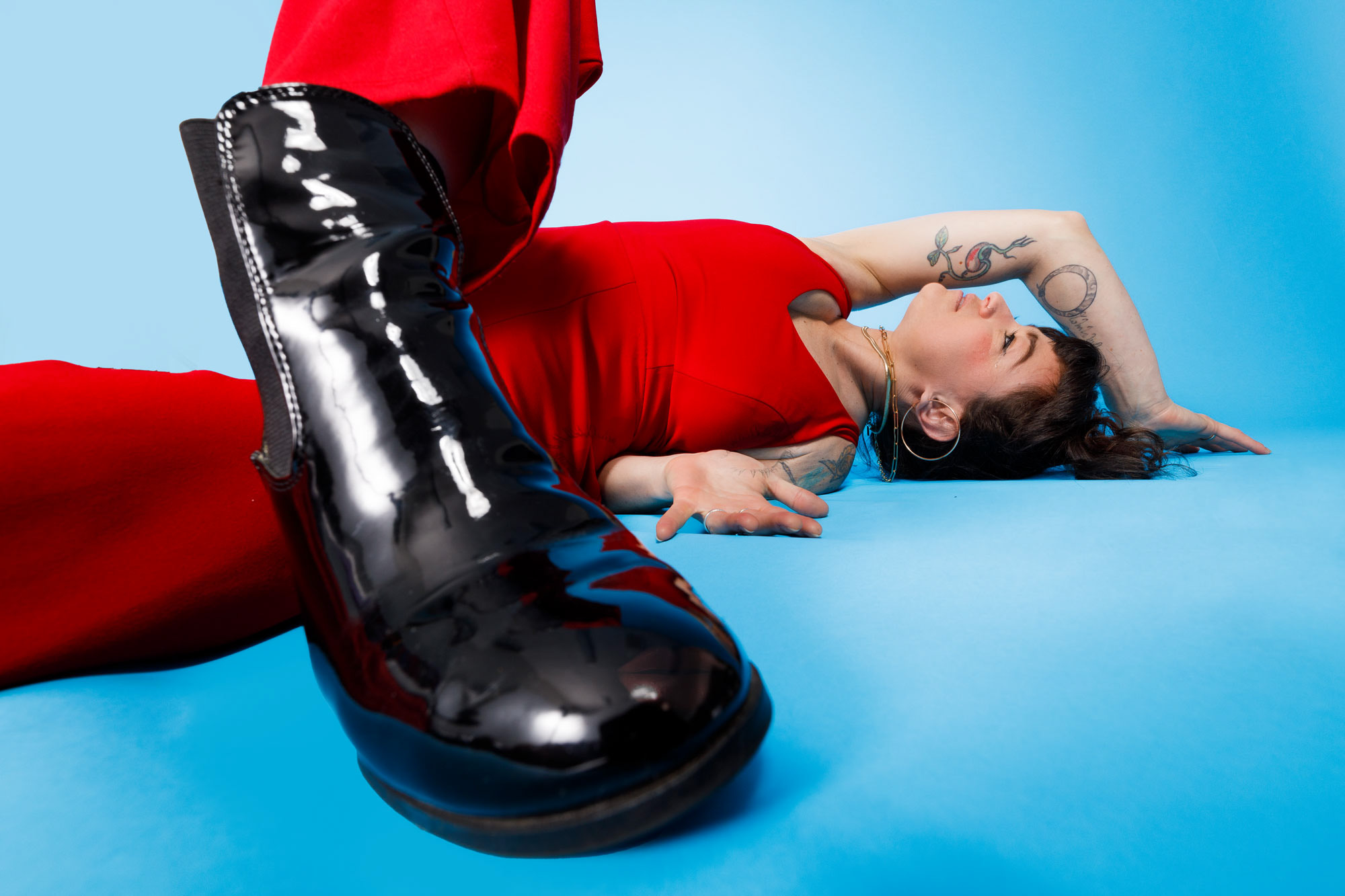 A person in a bold red outfit with striking black boots lying on a blue background, showcasing a confident and artistic pose.