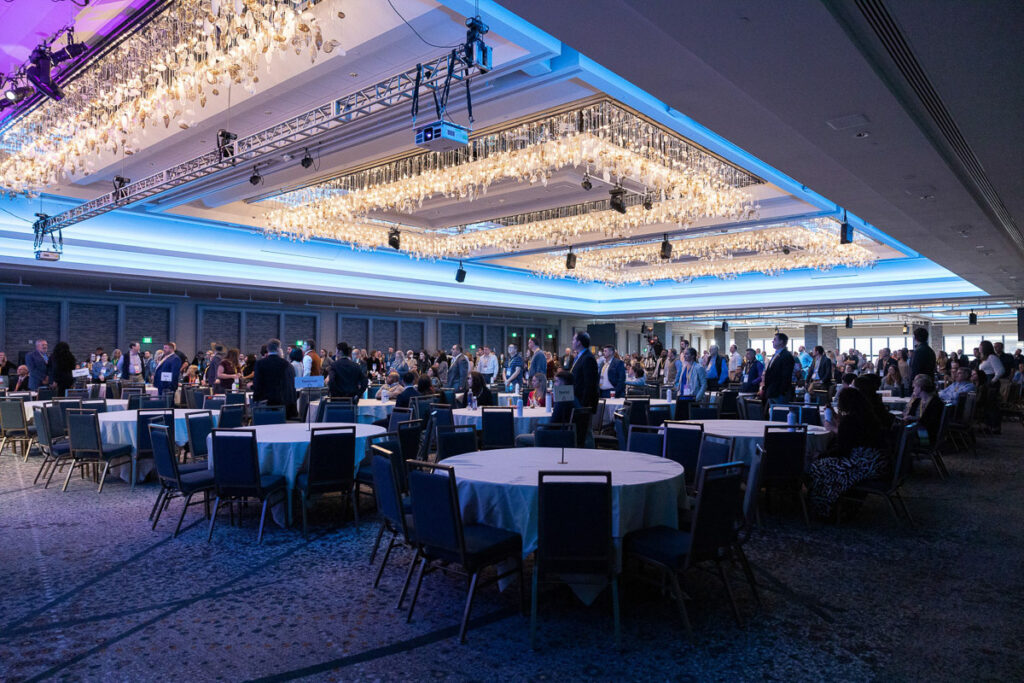 Professionals gather in an elegant banquet hall for a networking event, amidst sparkling chandeliers and arranged seating.