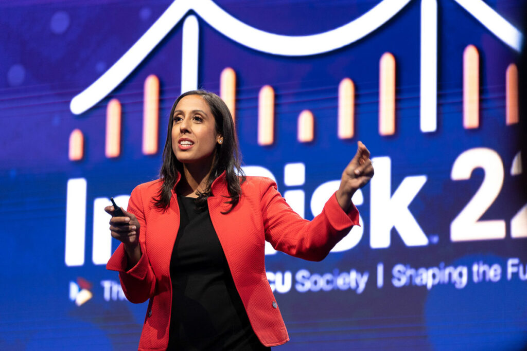 A confident speaker presents at a conference, with a dynamic graph in the background emphasizing growth, indicating a discussion likely focused on business or economic trends for the future.