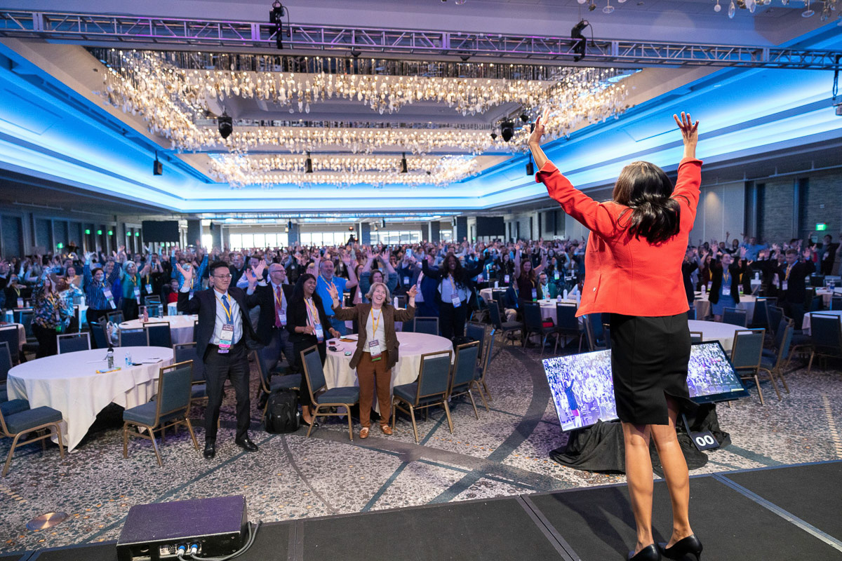 A motivational speaker receives a standing ovation from an engaged audience in a grand conference hall.