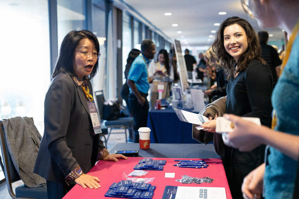 A professional interaction at a conference booth where a woman in business attire is engaging with a visitor, providing information and handing out materials.