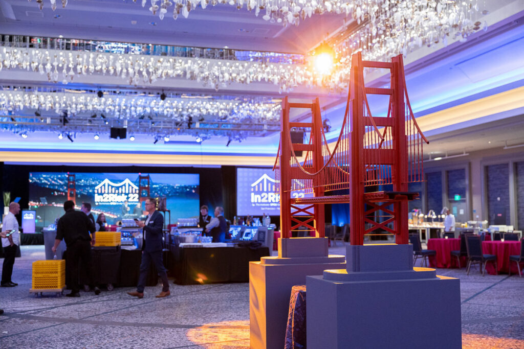 Elegant event hall with a theme featuring miniature models of a red suspension bridge, under a lavish crystal chandelier.