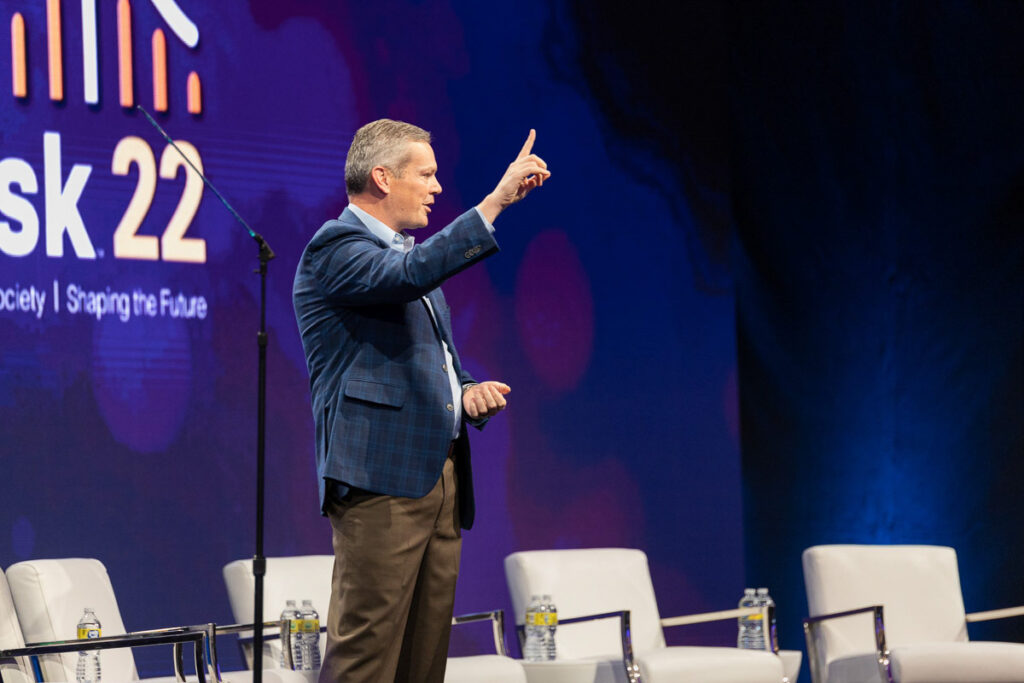 A speaker engaging with an attentive audience at the in2risk 22 conference event, set in an elegant venue with a large, colorful stage setup.