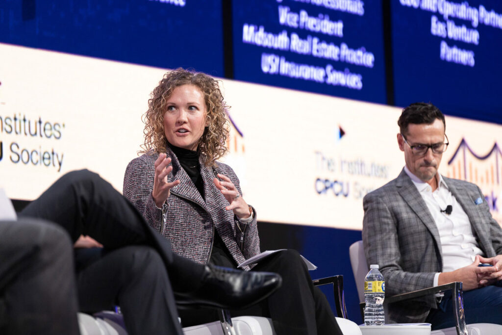 Aimee Kilpatrick engages the audience with a thought-provoking point during a panel discussion at a conference, as a male panelist listens attentively beside her.