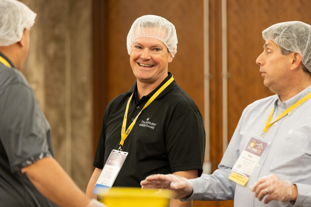 Volunteers wearing hairnets and gloves share a cheerful moment while preparing food at a community event.