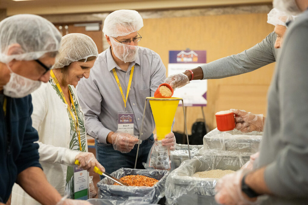 Volunteers in hairnets and gloves work together to prepare and package meals for a hunger relief effort.