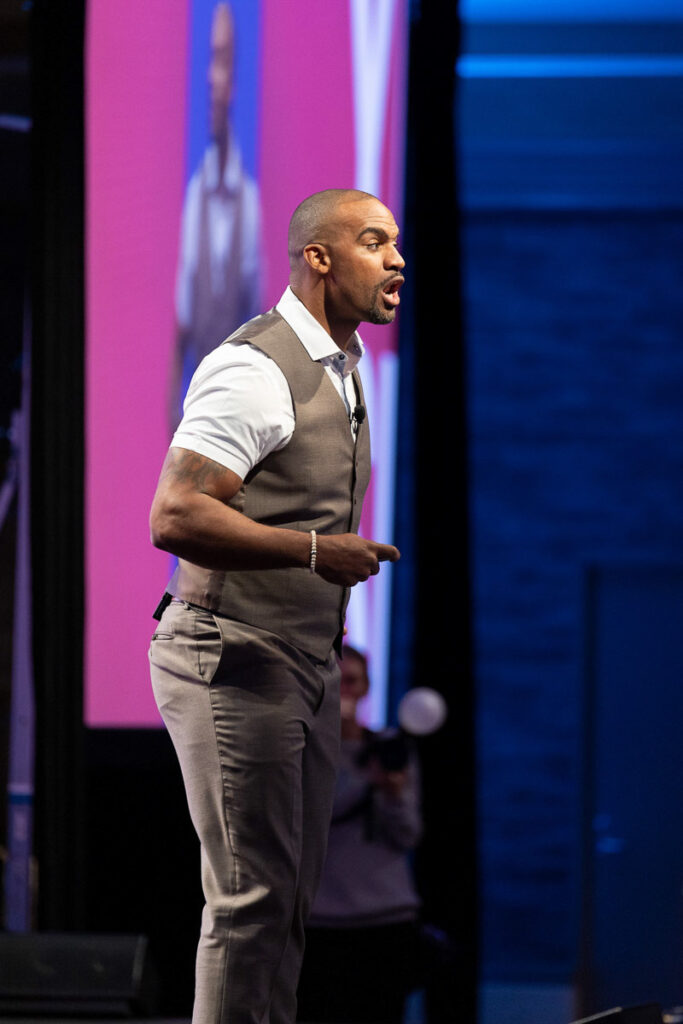 A motivated speaker gesturing confidently during an engaging keynote presentation on stage.