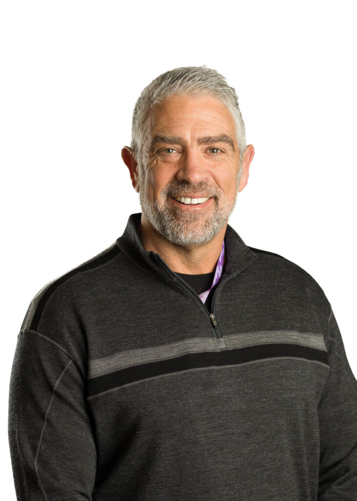 Mature man with a friendly smile, gray hair, and a casual pullover posing against a white background.