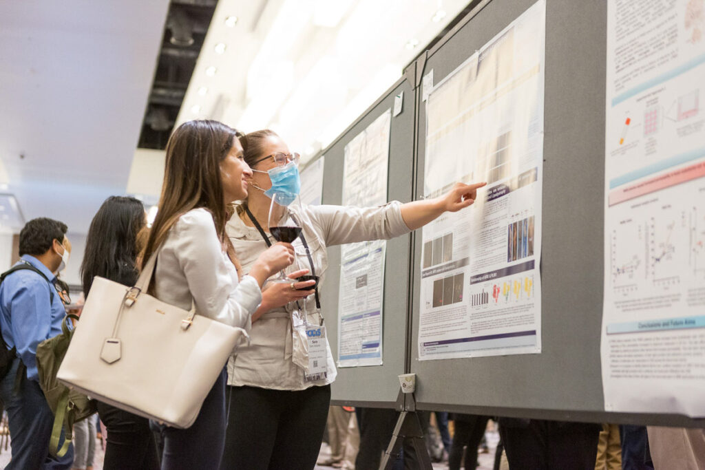 Two professionals engaged in discussion at a poster presentation session, with one pointing at details on a scientific poster.