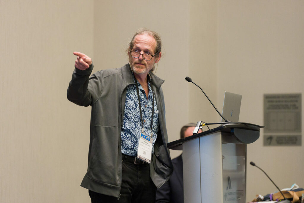 A confident speaker at a conference podium gesturing towards the audience, seemingly in the midst of an engaging presentation.