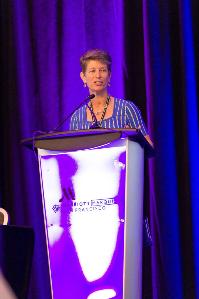 A woman delivering a speech at a podium with the Marriott marquis san Francisco logo visible.