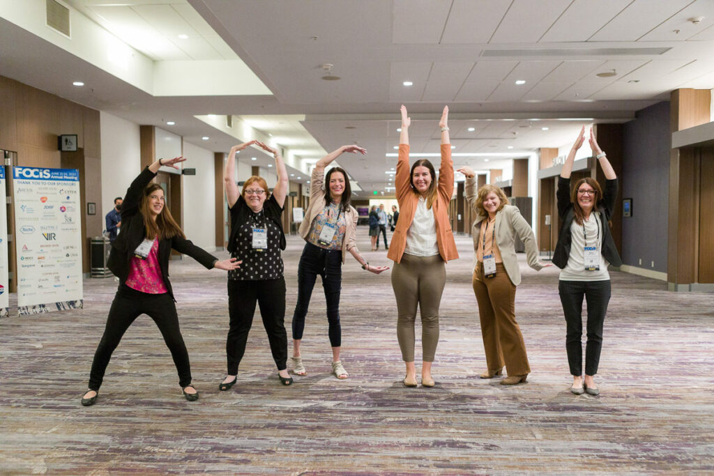 Group of cheerful people forming letters with their bodies in a conference hall setting.