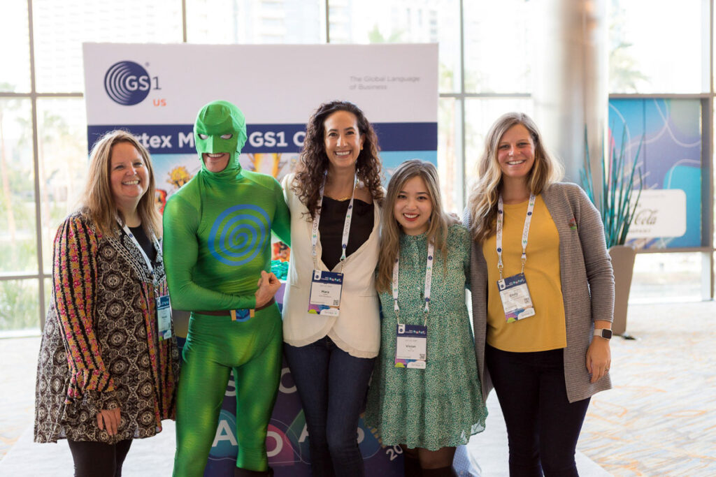 Group of smiling conference attendees posing for a photo with a person in a green superhero costume at the conference.