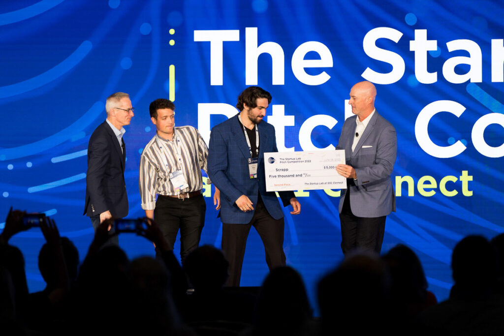 An entrepreneur receiving an award or recognition at a startup pitch competition, as attendees capture the moment on their devices.