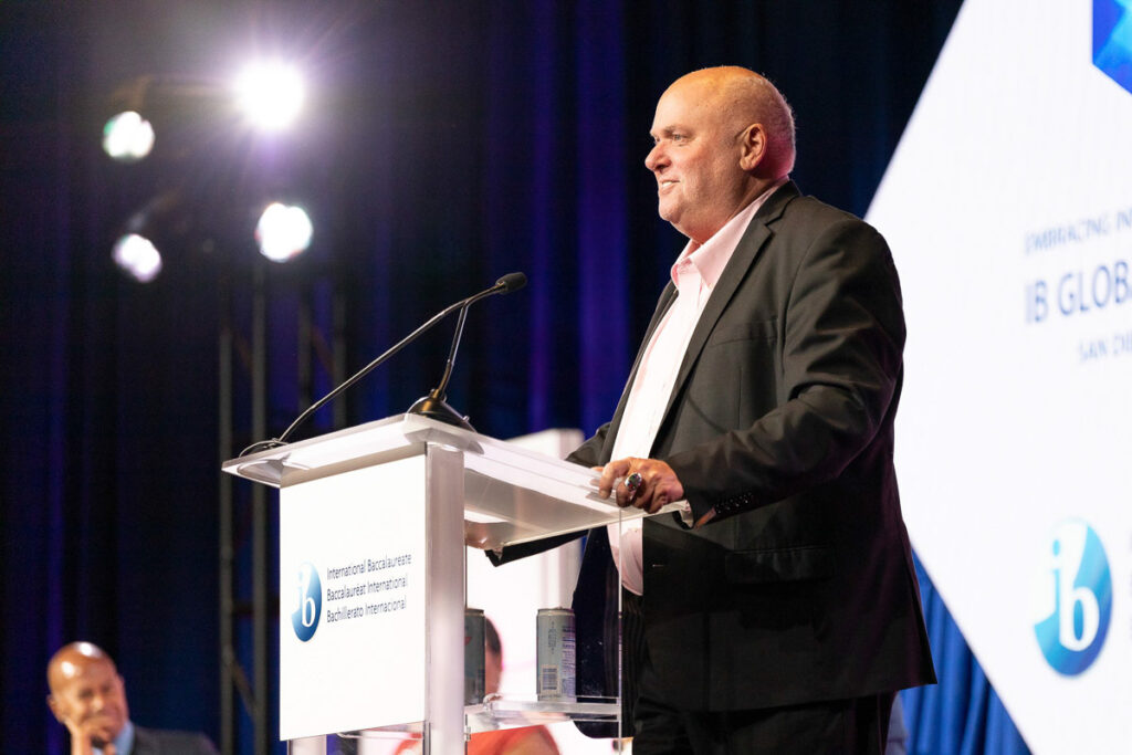 A speaker delivering a speech at a podium with a conference banner in the background.