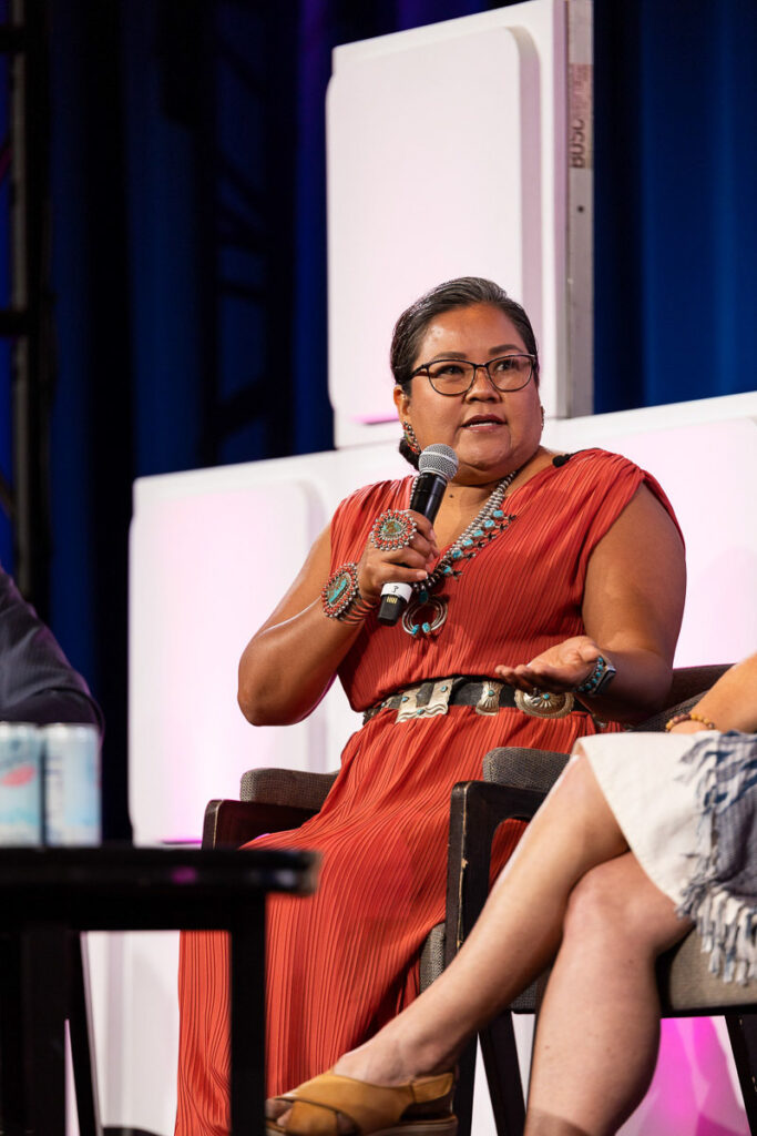 A confident speaker participating in a panel at a conference, engaged in delivering her perspective to the audience.