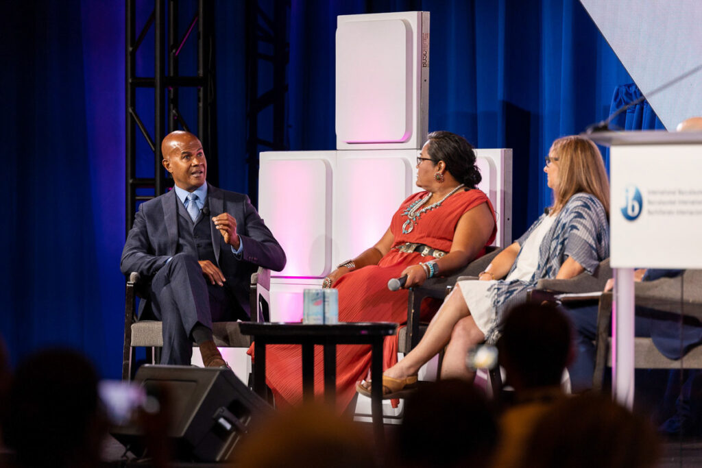 Three professionals engaged in a panel discussion at a conference, exchanging ideas in front of an attentive audience.