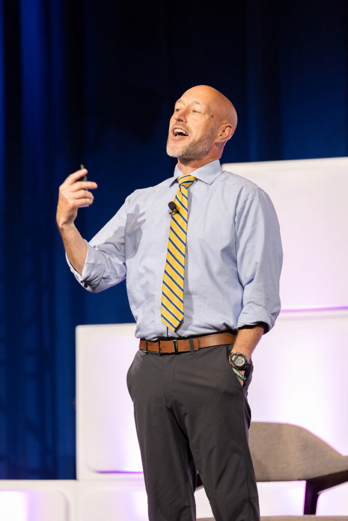 A keynote motivational speaker confidently addressing the audience with a passionate gesture at a conference.