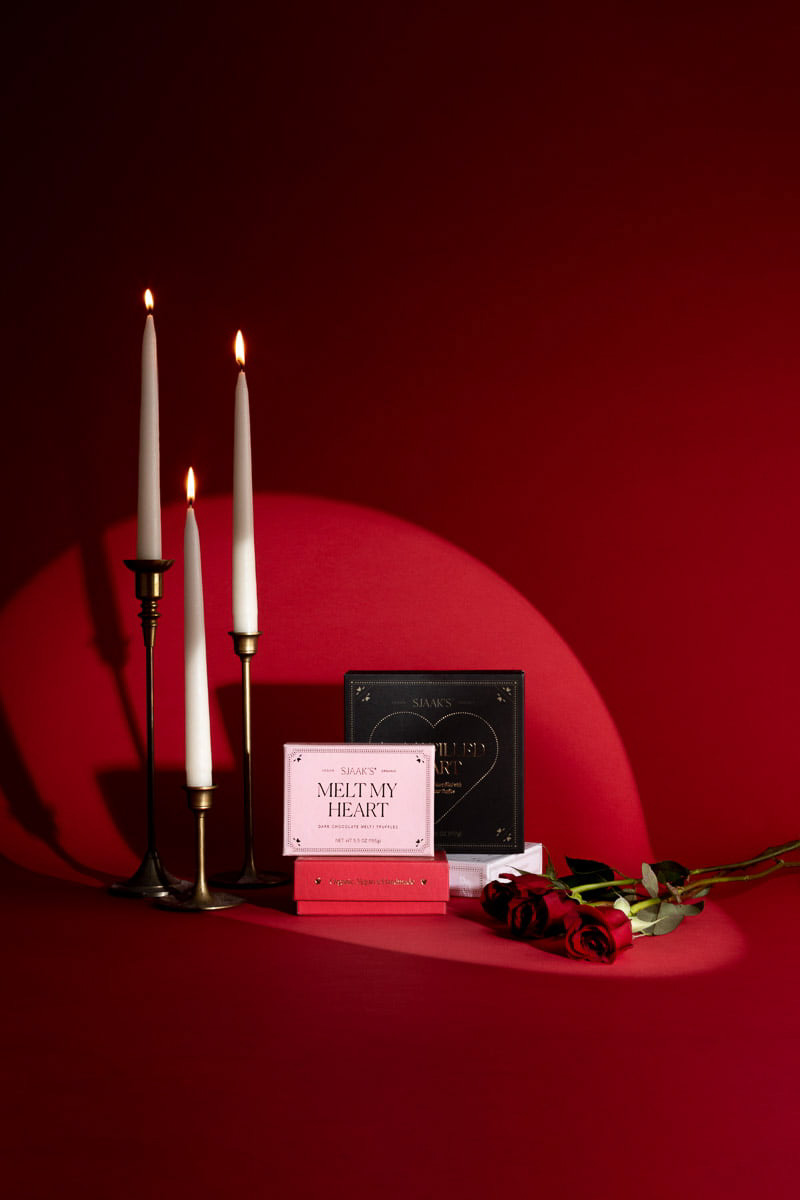 An elegant romantic setup with tall lit candles, a rose, and love-themed cards against a deep red background, creating an atmosphere of intimacy and celebration, perfect for product photography.