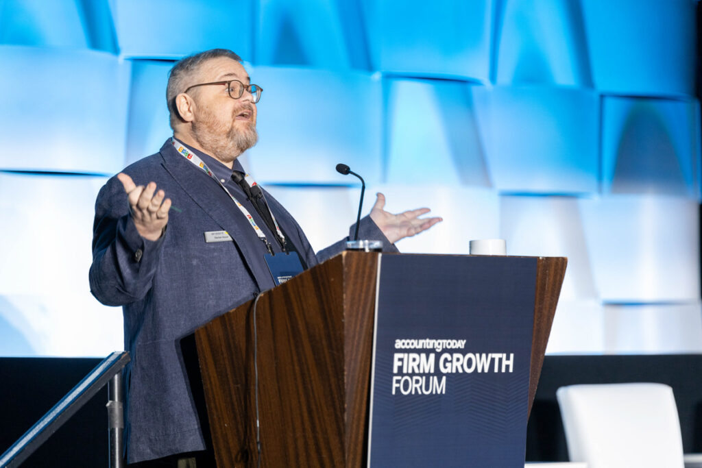 A man wearing glasses and a suit gestures while speaking at a podium labeled "accounting today firm growth forum" with a blue-lit geometric background.