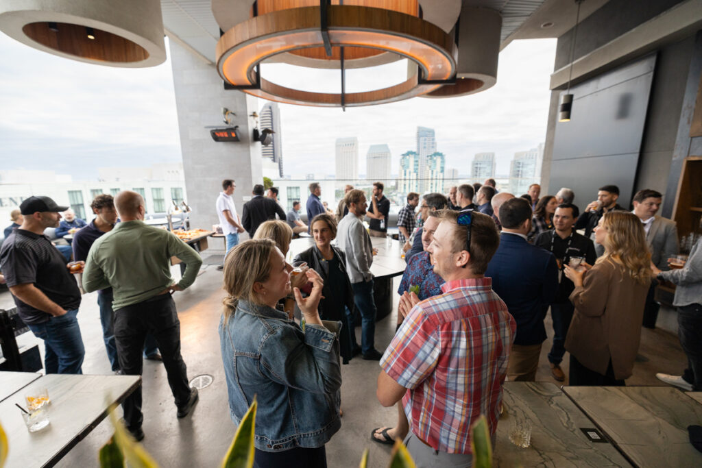 A lively networking event at a rooftop bar with a group of people chatting and enjoying drinks. the city skyline is visible in the background.